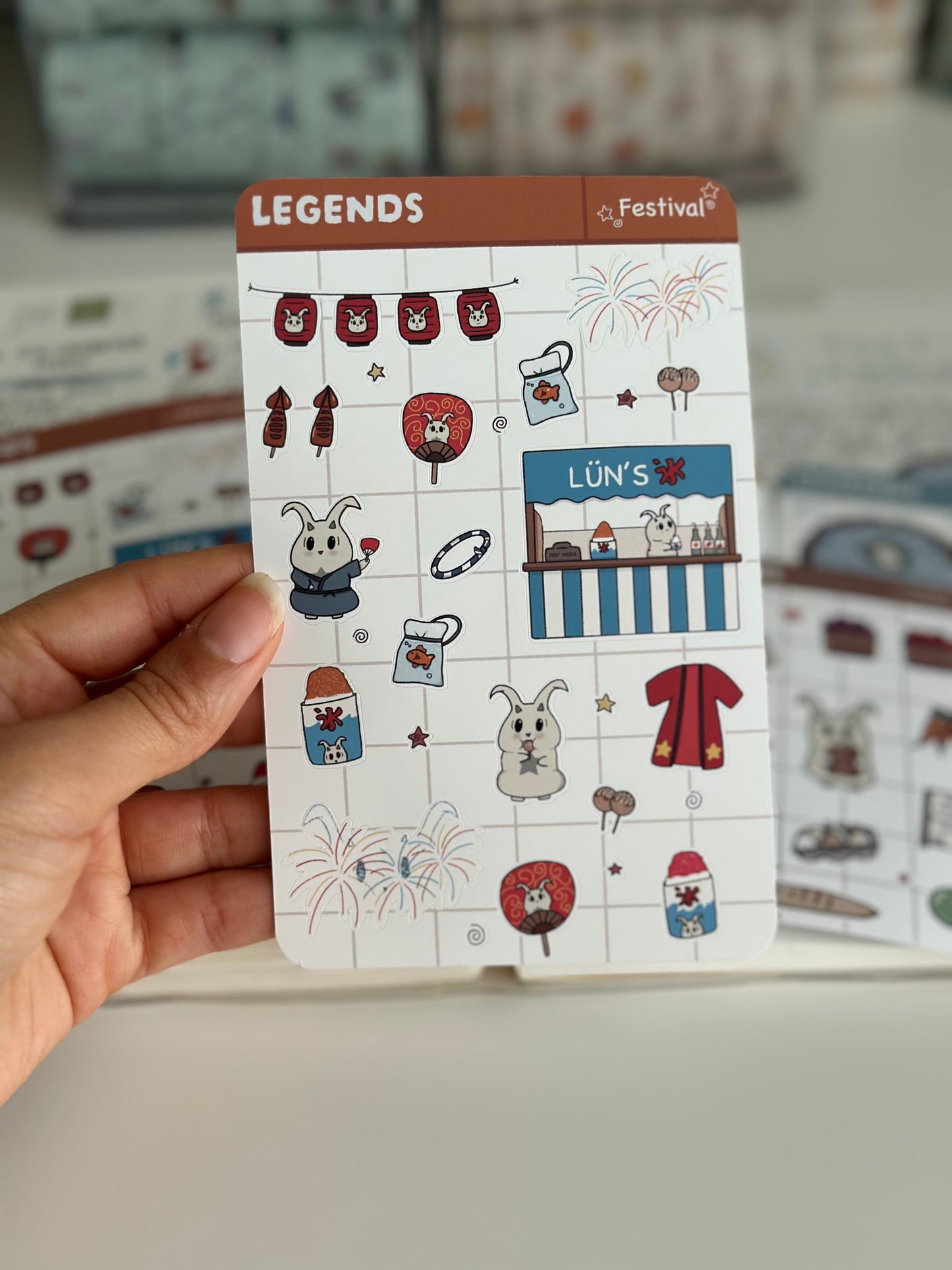 My hand holding the festival sticker sheet, that includes icees, fireworks, and more. 