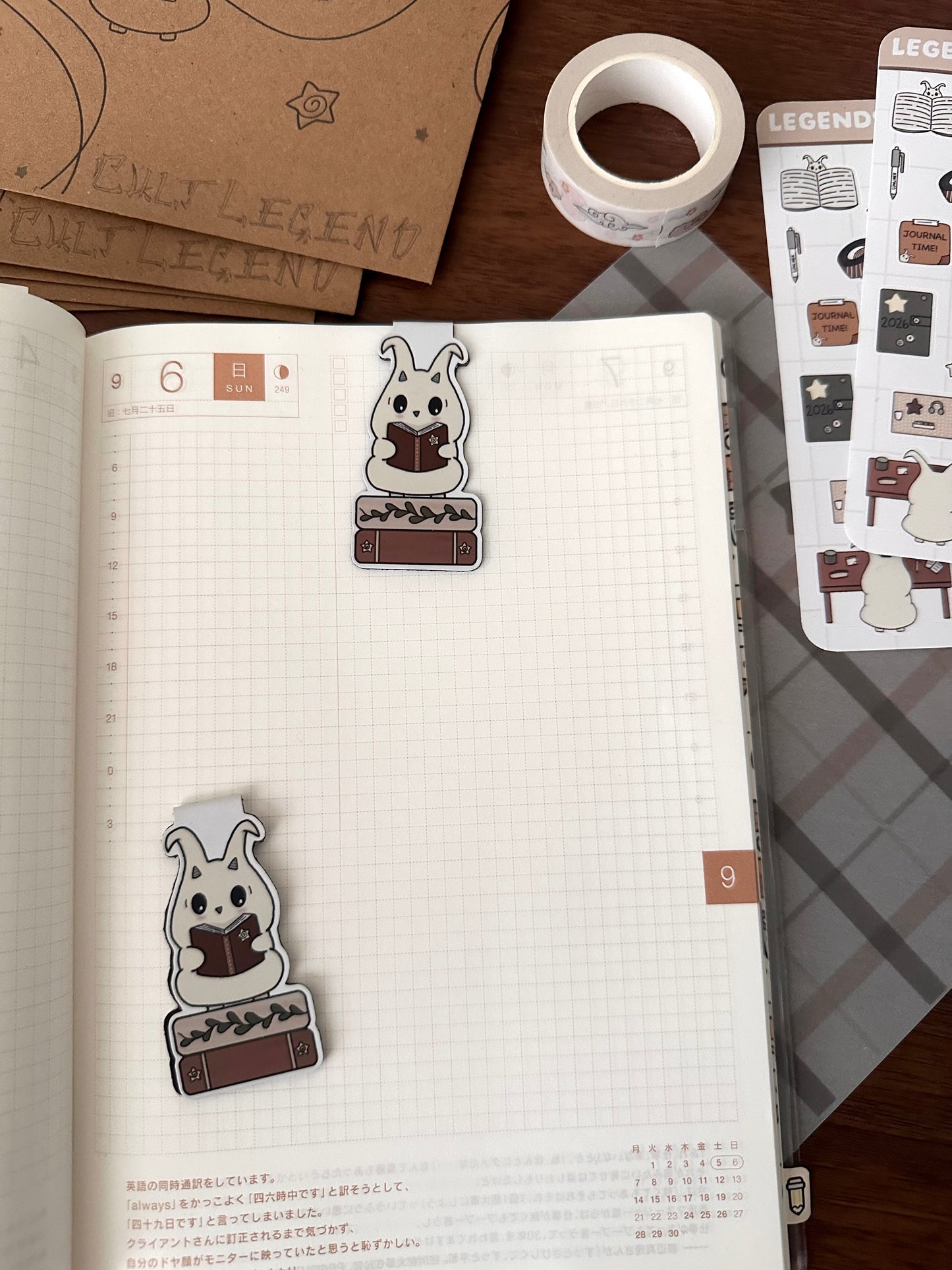 A planner or journal spread showing two cute lün bookmarks reading books, placed on white grid pages